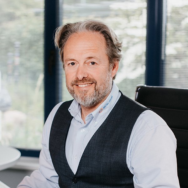 Der Mann mit einem gepflegten Aussehen und einem blauen Hemd strahlt Selbstbewusstsein aus, während er am Schreibtisch sitzt.