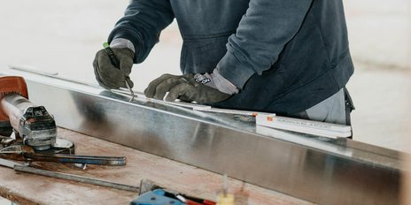 Mit einem Bleistift markiert eine Person mit Handschuhen sorgfältig eine Linie auf einem glänzenden Metallstück.