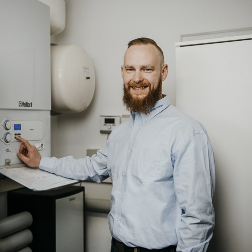 Der Fachmann mit Bart und freundlichem Gesicht bedient eine Heizungsanlage in einem modernen Raum mit neutralen Farben.