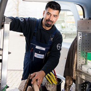 Ein freundlicher Handwerker in blauer Latzhose greift nach einer Kiste, um seine Ausrüstung für den Tag vorzubereiten.