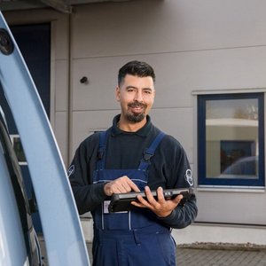 Der Techniker in blauer Arbeitskleidung nutzt ein Tablet, während er vor einem modernen Gebäude steht.