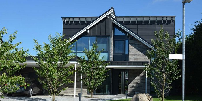 Die Fassade eines stilvollen Hauses mit großen Fenstern und einem eleganten Dach, umgeben von grünem Laub.