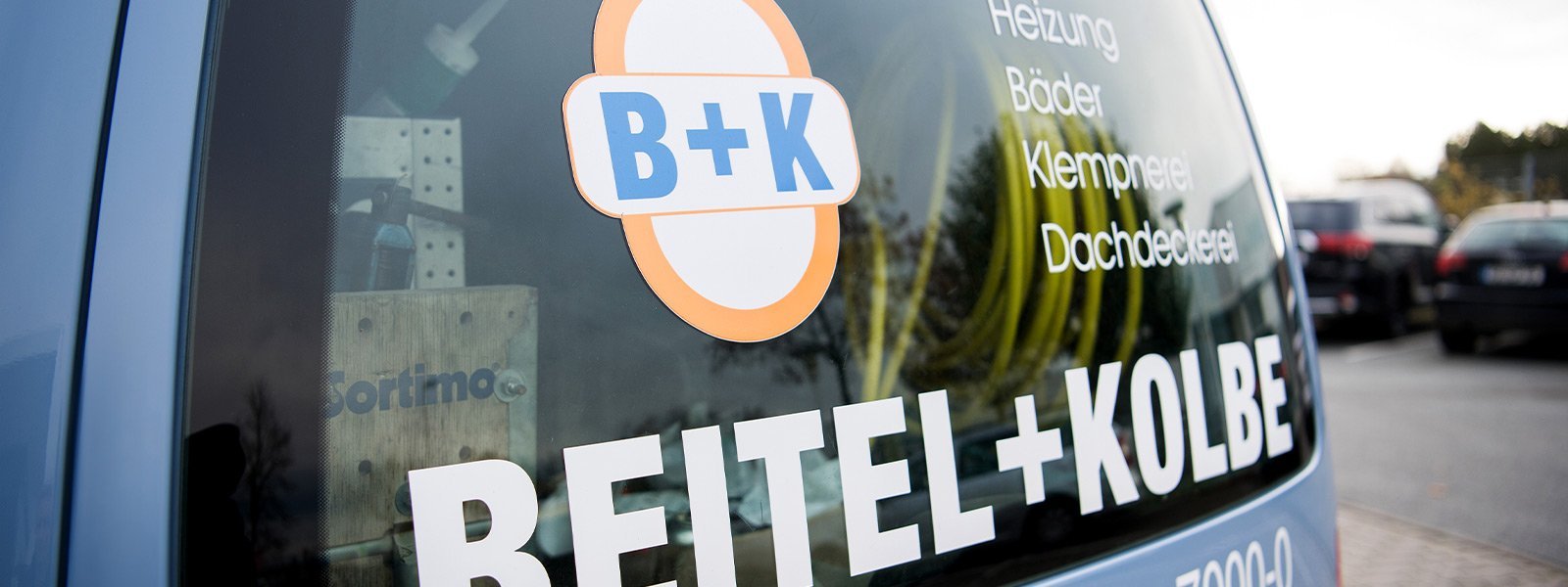 Die Rückseite eines Handwerkerfahrzeugs zeigt das Logo B+K sowie die angebotenen Dienstleistungen in klarer Schrift.