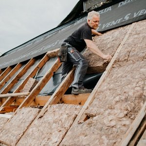 Ein Mann in Arbeitskleidung installiert Dämmung auf einem Dach, um die Isolierung zu verbessern.