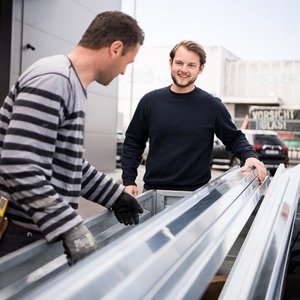 Die beiden Männer scheinen an einem Projekt zu arbeiten, während sie sich gegenseitig anlächeln und konzentriert sind.