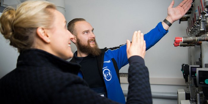 Der Mann zeigt mit einer Hand auf eine technische Vorrichtung, während die Frau interessiert zuhört und lächelt.
